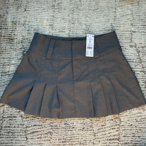*NYSKICK* Grå platerad kjol från Gina Tricot - Grå platerad kjol i storlek M från Gina Tricot. Helt ny och aldrig använd. Säljs p.g.a för stor storlek. Ursprungspris 369 kr.