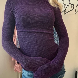 Lila polotröja - En figursydd lila polotröja med långärmade ärmar. Tröjan har ett subtilt mönster och är tillverkad i ett stretchigt material som ger en bekväm passform. Köptes på Sellpy för cirka 100kr, men aldrig använd av mig. Tröjan har ej bucklor på handlederna, jag har armband under tröjan på bilden. perfekt till fest.
