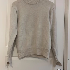 Beige stickad tröja från H&M - En beige stickad tröja från H&M med en ribbad polokrage. Tröjan har långa ärmar och ribbstickade muddar vid ärmslut och nederkant. Perfekt till hösten!