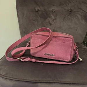 Jacquemus väska - Modell: Le baneto suede Färg: rosa Skick: bra, sparsamt använd, inga trasiga anmärkningar, enbart lite missfärgning på mockat på kanterna av väskan (se bilder) Köpt på Vestiaire collective Material: mocka/suede Mått: H 10,5 cm B 18,5 cm D 6,5 cm 