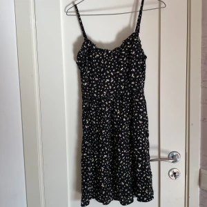 Blommig klänning - Jättegullig blommig, svart klänning från Divided/H&M i stl 36🥰  Något volangernad i kanterna på framsidan, stretchiga resår på ryggen(se bild).  Blommorna är i vitt, gult och rosa med gröna små blad. 💓