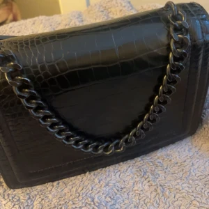 Svart väska - En medelstor svart väska med tjockt band, bra skick. Den är från utomlands så vet inte riktigt vilken butik eller så.