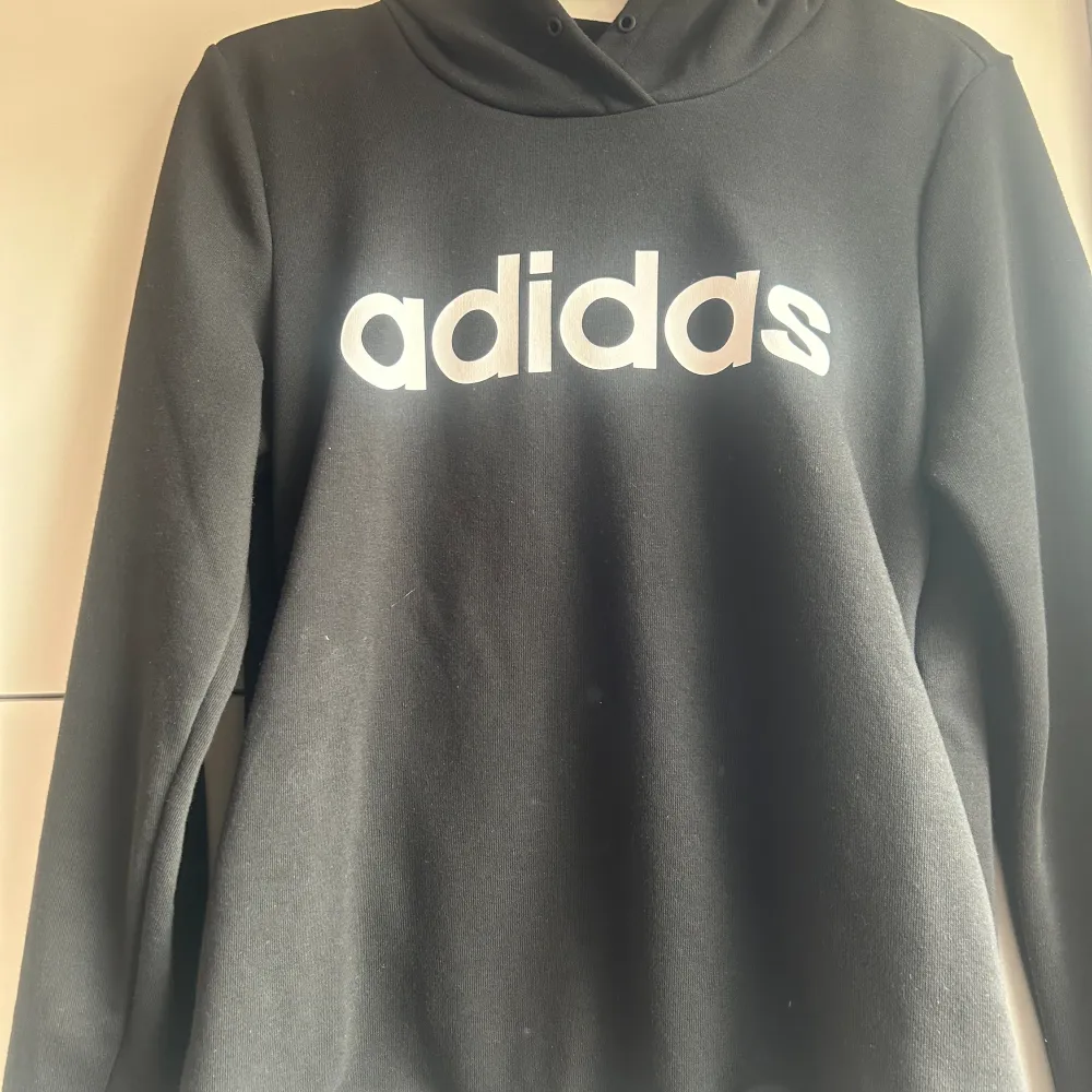 En svart adidas hoddie med luva, den har även fickor. Snören är tyvärr av. Använd ett par gånger men är i bra skick. Storlek S. Hupparit & Collegepaidat.