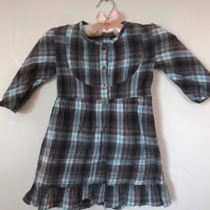 Rutig klänning  - Fin rutig klänning i grått och blått. Har knappar vid halsen man kan knäppa upp när den ska tas på eller av. Är i fint skick. Från märket GIRLS WEAR i storleken 122. 