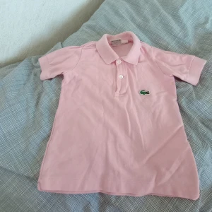 Tshirt  - Säljer en rosa Lacoste polo. Storlek 98 (3åring). Mycket bra skick, använd ca 2 gånger. Originalpris ca 600kr. Jag säljer den för 180kr + frakt!