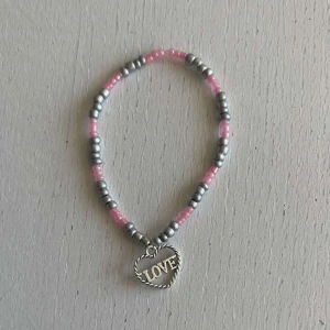 Egengjort armband  - Ett egengjort pärlarmband med färger av silver och rosa. Armbandet har en silvrig berlock som avbildar ett hjärta med ordet ”Love” inuti. 