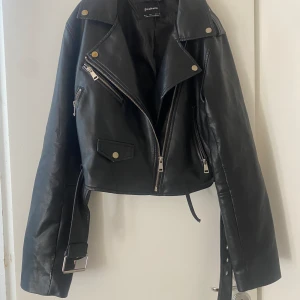 Skinnjacka  - Svart skinnjacka, väldigt snygg. Tyvärr så som ni ser har den gått sönder där nere(den som hänger ner vet inte vad den heter) går att fixa antingen klippa bort den eller limma fast den🫶🏼