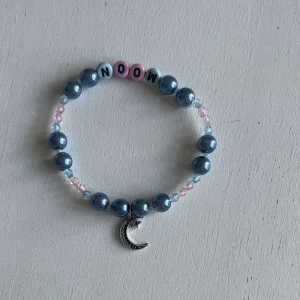 Egengjort pärlarmband  - Ett egengjort pärlarmband med färgerna blåögd rosa i olika nyanser med en blandning pärlsorter. Armbandet har en berlock i silver som avbildar en måne och pärlor med bokstäver som avbildar ordet ”Moon”.