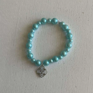 Egengjort pärlarmband  - Ett egengjort pärlarmband med färgeren blå med en blandning pärlstorlekar. Armbandet har en berlock i silver som avbildar en ros. 