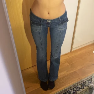 Lågmidjade jeans - Lågmidjade blåa jeans med coola detaljer från Nelly. Använda en gång så är precis som nya. Storlek: 38. Innerbenslängd: 81 cm. Inköpspris: 699 kr. 