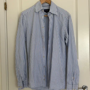 Eton skjorta - Detta är min brors blå och vit randiga skjorta av märket Eton. Han vill sälja den eftersom han har vuxit ur den. Den har inga defekter utan är i mycket gott skick. Skjortan är somrig och passar perfekt under sommaren!