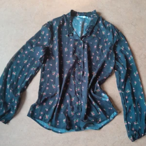 Semi-transparent Blus - En svart blus med små röda blommor, i semi-transparent mesh tyg. Knappar fram och väldigt söt veckad krage. Storlek L, men sitter bra, lite oversize, på mig som vanligtvis har S/M. Helt ny, har inte blivit av att jag använt tyvärr.