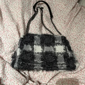 Rutig väska - Säljer denna supersöta väska då den inte kommer till användning. Fint skick då den endast använts en gång. Går att ha med lång eller kort kedja. Har ett stort fack och även ett litet med dragkedja. Skriv för frågor 🧡