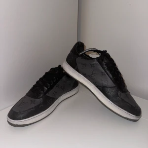 Louis Vuitton rivoli sneakers St: 42 - Ett par Louis Vuitton Rivoli sneakers storlek 42 i använt skick men ser fortfarande bra ut. Det finns ett litet hål i högra skon som man kan se i en av bilderna. Hålet syns knappt vid användning. Nypris ca 10000kr, mitt pris 3999. Finns kvitto