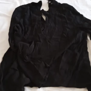 Svart blus strl 40 - Tunn Svart blus som trär över huvudet. Strl M , breda ärmslut, 100% viskos. Knäpps med 2 knappar i nacken. 