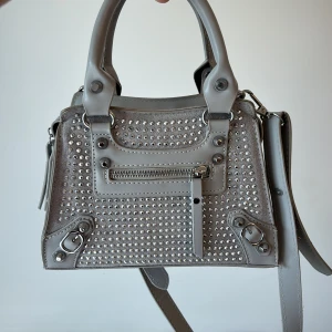 Grå väska med strass  - Jättefin väska axelband. Inköpt i våras och endast kommit till användning ett fåtal gånger. Topp skick