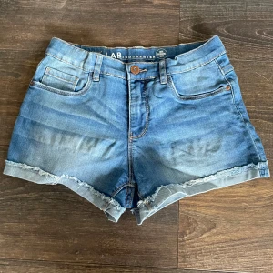 Blåa jeansshorts - Blåa jeansshorts som har mellanhög midja, med justerbar resår runt midjan. Välanvända men i väldigt sparsamt och gott skick. 