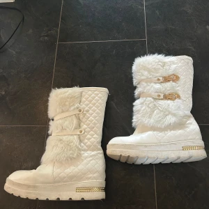 Vita quiltade stövlar med päls och spännen - Säljer ett par supercoola vita stövlar med quiltat mönster och fluffig pälsdetalj. De har två guldfärgade spännen och en rad med guldfärgade nitar längst ner på sulan. Perfekta för vintern och håller dig varm och snygg! 🥰