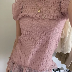 Ljusrosa spetsklänning från H&M - Säljer en superfin ljusrosa spetstopp från H&M i storlek XS. Toppen har ett vackert spetsmönster och volangdetaljer vid ärmarna och nederkanten. Den är ärmlös och perfekt för sommarens alla fester. Toppen är i nyskick och har en tight passform💖