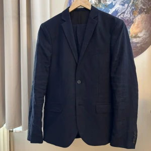Mörkblå kostym från H&M - Säljer en snygg mörkblå linnekostym från H&M Premium i storlek M. Kavajen och byxorna är i nyskick och har en klassisk design med två knappar fram och fickor. Perfekt för både fest och bal. Materialet ger en elegant look.