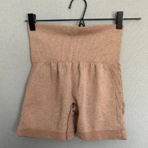 Beiga högmidjade shorts - Säljer ett par beiga högmidjade shorts. De är superbekväma och perfekta för träning eller bara att chilla i. Materialet känns mjukt och stretchigt, vilket gör dem riktigt sköna att ha på sig. Passformen är tight och de sitter bra på kroppen.