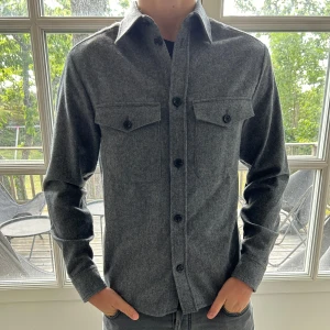 J.Lindeberg Overshirt - Vi säljer nu denna sjukt snygga overshirten i ull, från J.Lindeberg. Skick: oanvänd (lappen kvar). Storlek S men passar M. Modellen är 185 och väger 75kg. Nypris: 3400kr, vårt pris: 999kr! Tveka inte på att höra av dig vid frågor.