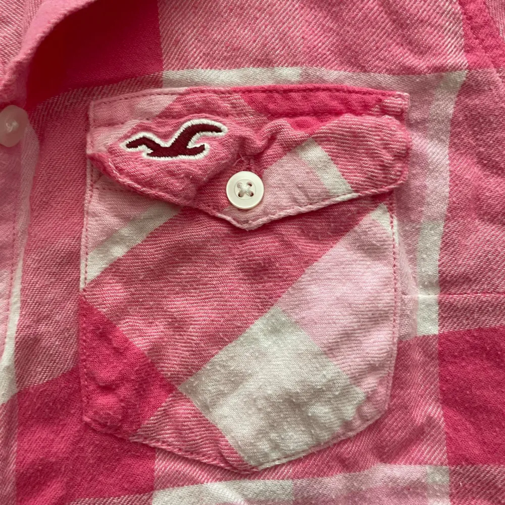 En rutig skjorta från Hollister i rosa och vit. Skjortan har långa ärmar och två bröstfickor med knappar. Den är tillverkad i bomull och har en normal passform.. Skjortor.