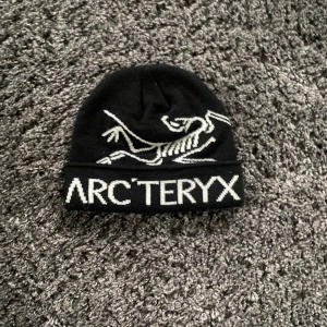 Arcteryx Mössa - En svart Arcteryx mössa med vit text och deras egna fosil motiv. Mössan är i fint skick och har använts fåtal gånger i vintras. Den är självklart äkta och tags och allt finns. Köpt från usa. Skriv pm för frågor eller fler bilder 👌 