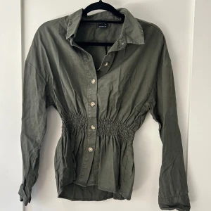 Mörkgrö Tröja  - Strechig i midjan. Lite större puffiga ärmar. Knappar fram.  Storlek 38