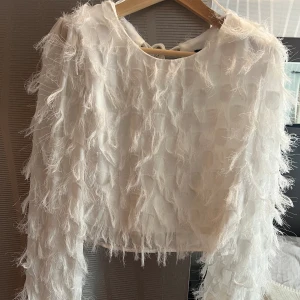 Blus med fransar  - Vit blus från Ginatricot med fransar och knytning baktill samt vadderade axlar. Använd en gång. Storlek S. 