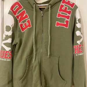 Plus eighteen hoodie  - Rkt cool army Green hoodie med rött text och dödskalle på armarna. Inga defekter 