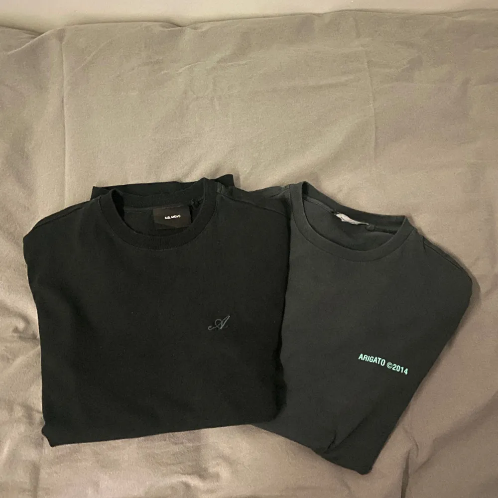 Två gamla arigato t-shirts som inte passar mig längre. Helt vanlig passform, varken tight eller oversized. Ingen av tröjorna har fläckar eller skador. Den gråa har ljusblå text fram och bak. Den svarta har ett stickat märke på framsidan.. T-paidat.