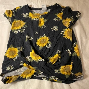 En svart T-shirt med solrosor på - 128cm  Använt få gånger är fortfarande i bra sick  Köparen står frakten