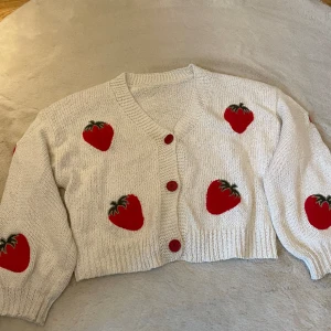 Stickad vit kofta med jordgubbar  - En supersöt kofta, lång i armarna, knappar och söta jordgubbar på! 