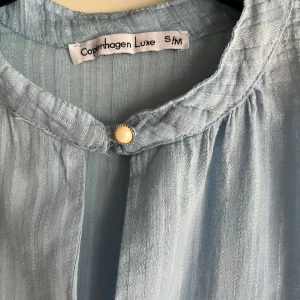 Blus i nyskick  - Blus av fint märke. 100 % tunn, skir  bomull med silvertrådar, 3/4 ärm, pärlknappar.  Använd ett fåtal tillfällen. Snygg till kostymbyxor.  Köparen betalar frakt. 