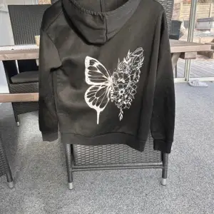 Svart hoodie med fjärilstryck på ryggen. Den är nopprig då den är använd men ändå i fint skick.