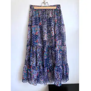 Blå blommig kjol i chiffong med volanger, bred elastisk linning. Mått i cm: midjevidd 36; längd 91.