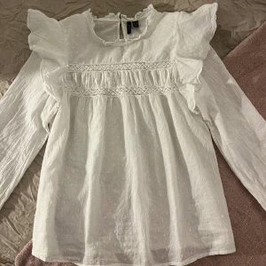 Vit blus med volang och broderi - Vit blus från vero Moda med volang och broderi. Liten i storlek så skulle säga att den är storlek S. Aldrig använd! 