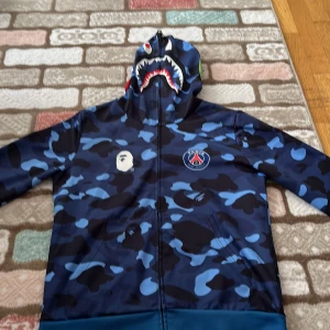 Bape Hoodie - Bape är ett av de bästa säljande märke i världen. Artister som xxxtentacion Kanye West är bara en av dem som har bape.  Denna bape är en samarbete med Psg så denna är värkligen cool.