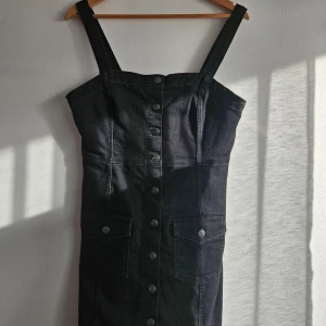 Jensklänning  - Säljer en svart jensklänning. Klänningen har breda axelband, en rak urringning och en stilren knappslå med knappar hela vägen ner.Perfek för både vardag och festliga tillfällen! Jag har bara använt den en gång.Hör av dig om du är intresserad! 