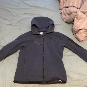Mörk blå Nike tech fleece - Nike hoodie köpt från deras hemsida, den har ett jättelitet hål vid ena ärmen som man inte tänker på. Skick 9/10 storlek s men passar även m. Nypris: 1400