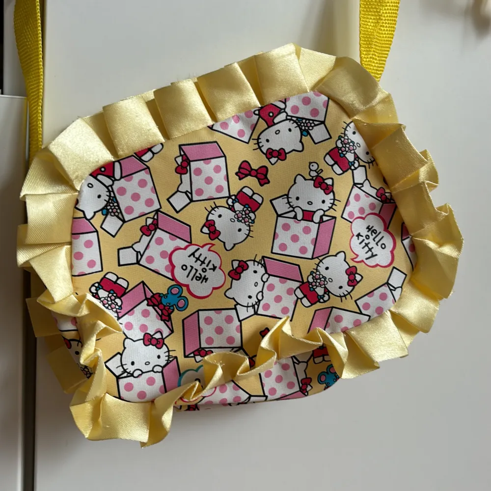 Supersöt väska med Hello Kitty-motiv. Stängs med dragkedja. Gul lång axelrem. Storlek 20x15 cm. . Väskor.