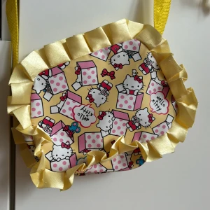 Väska Hello Kitty - Supersöt väska med Hello Kitty-motiv. Stängs med dragkedja. Gul lång axelrem. Storlek 20x15 cm. 