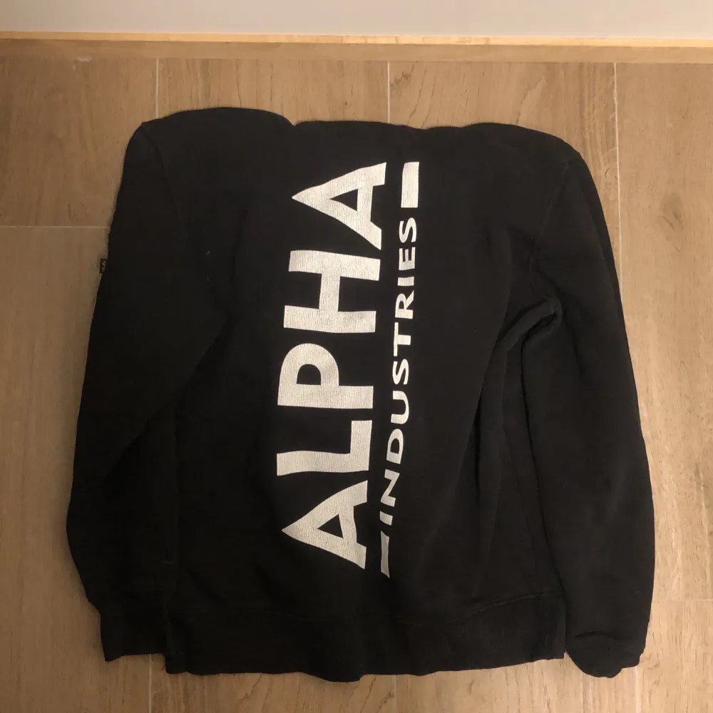 En svart hoodie från alpha industries. Vitt tryck på ryggen och luvan. Sparsamt använd . Hoodies.