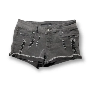 Grå jeansshorts med slitningar - Från HotTopic Storlek: 0 Midja: ca 73cm Längd: 21,5cm (sidan) Ett par grå jeansshorts med slitningar och fransiga kanter. Shortsen har fem fickor och en knapp- och dragkedjestängning framtill.