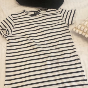 Randig t-shirt från KappAhl - En vit och svart randig t-shirt från KappAhl. T-shirten har korta ärmar och en rund halsringning.💓😽