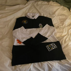 Stilig piké ända från LA - Vintage svart och vit randig piké med olika sy-på tryck. Storlek L. Aldrig använd. Från Cross Colours i Los Angeles ”Designed With Pride”. PRIS KAN DISKUTERAS!