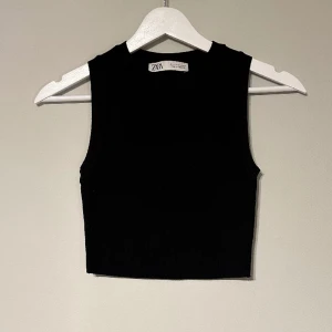 Svart Zara topp - Ett svart linne från Zara i storlek S. Linnet är croppad och har en ganska hög rund krage. Dessutom är det ett tjockt och lyxigt ribbat tyg. 