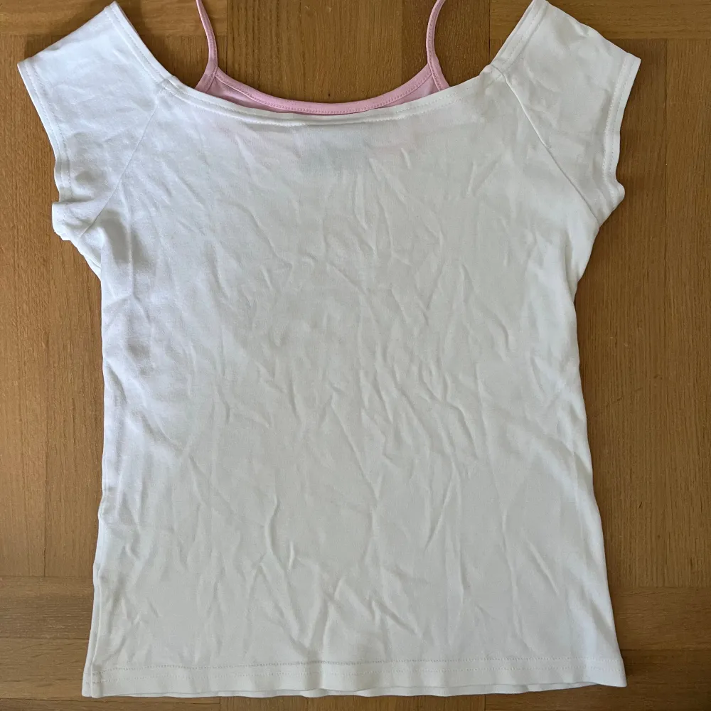 Vit barn t-shirt med katt gjort av strass. Med rosa knytband i nacken. Stolek: 158/164. T-paidat.