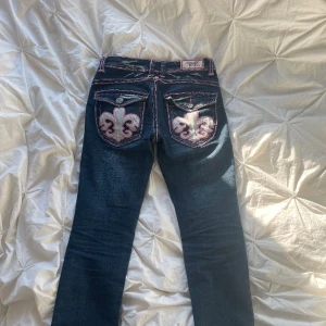 Y2k lågmidjade Laguna Beach jeans med snyggt tryck - lågmidjade jeans, köpte här på plick för ett tag sedan. Säljer då det inte är min stil längre. Coolt tryck på bakfickorna. Passar mig som har XS/S. Midja:27 Innerben:82 Lite bootcut. Bra kvalite förutom knapparna på bakfickorna, men inget som syns.